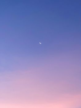 A calming view of a crescent moon in a pastel sky during twilight.