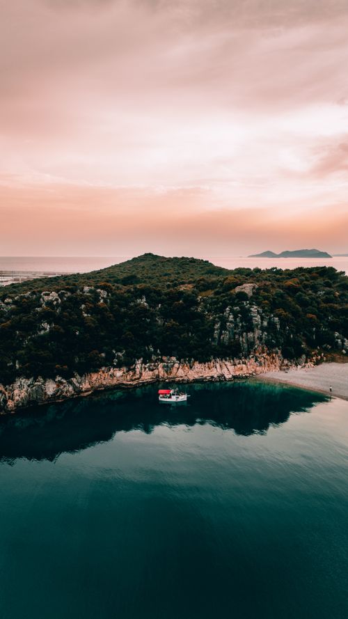 Free Stunning aerial view of Antalya's coastline with serene waters and lush greenery under a pink sunset. Stock Photo