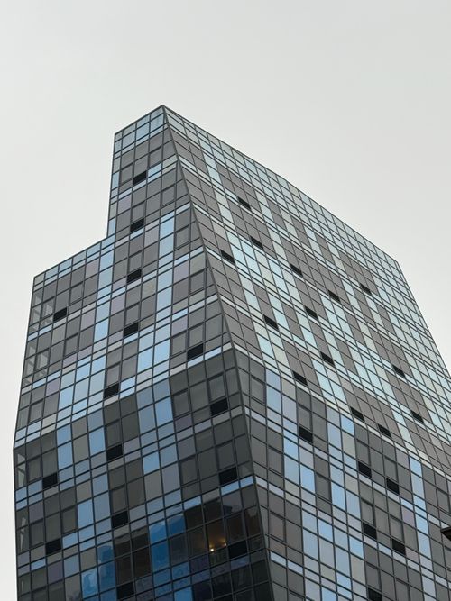 Free Close-up of a modern glass skyscraper with geometric design against a cloudy sky. Stock Photo