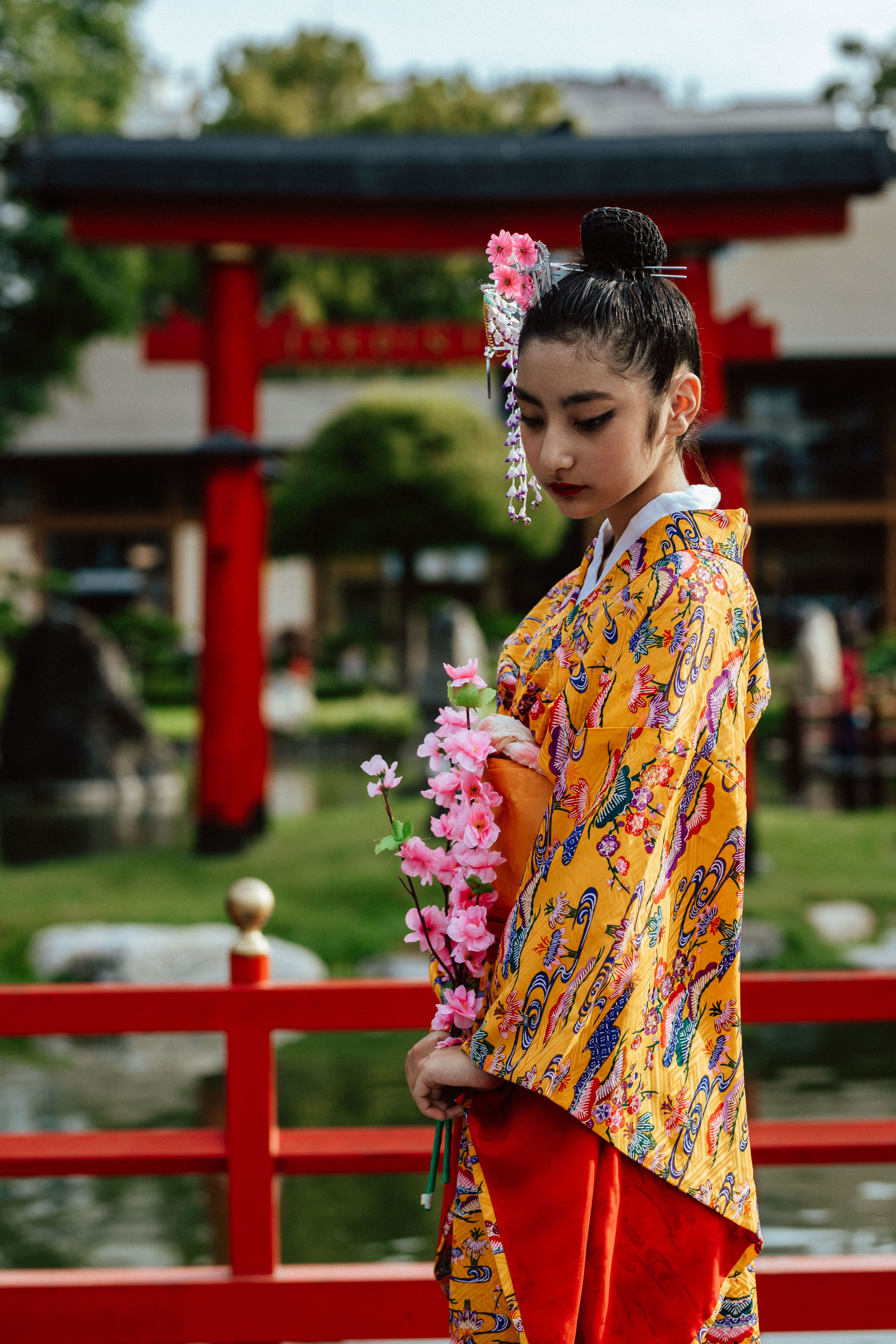 A serene portrait of a woman in a kimono holding flowers in a traditional Japanese garden setting.