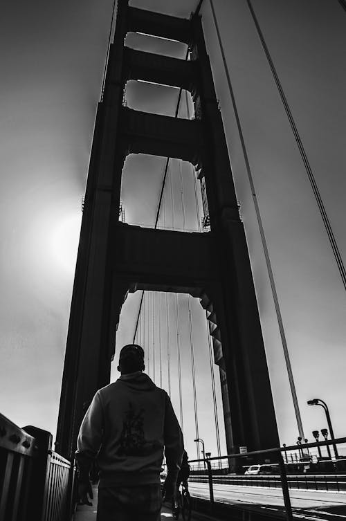 Monochrome Photo of Man Walking in Suspension Bridge