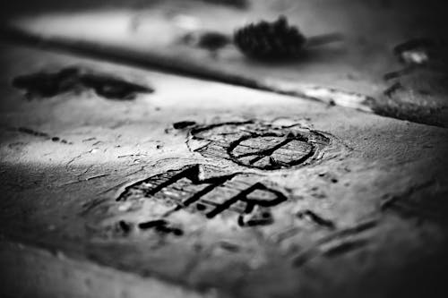 From above closeup black and white of old rectangular wooden planks with uneven shabby surface and cut out letters near circle with lines inside in daylight