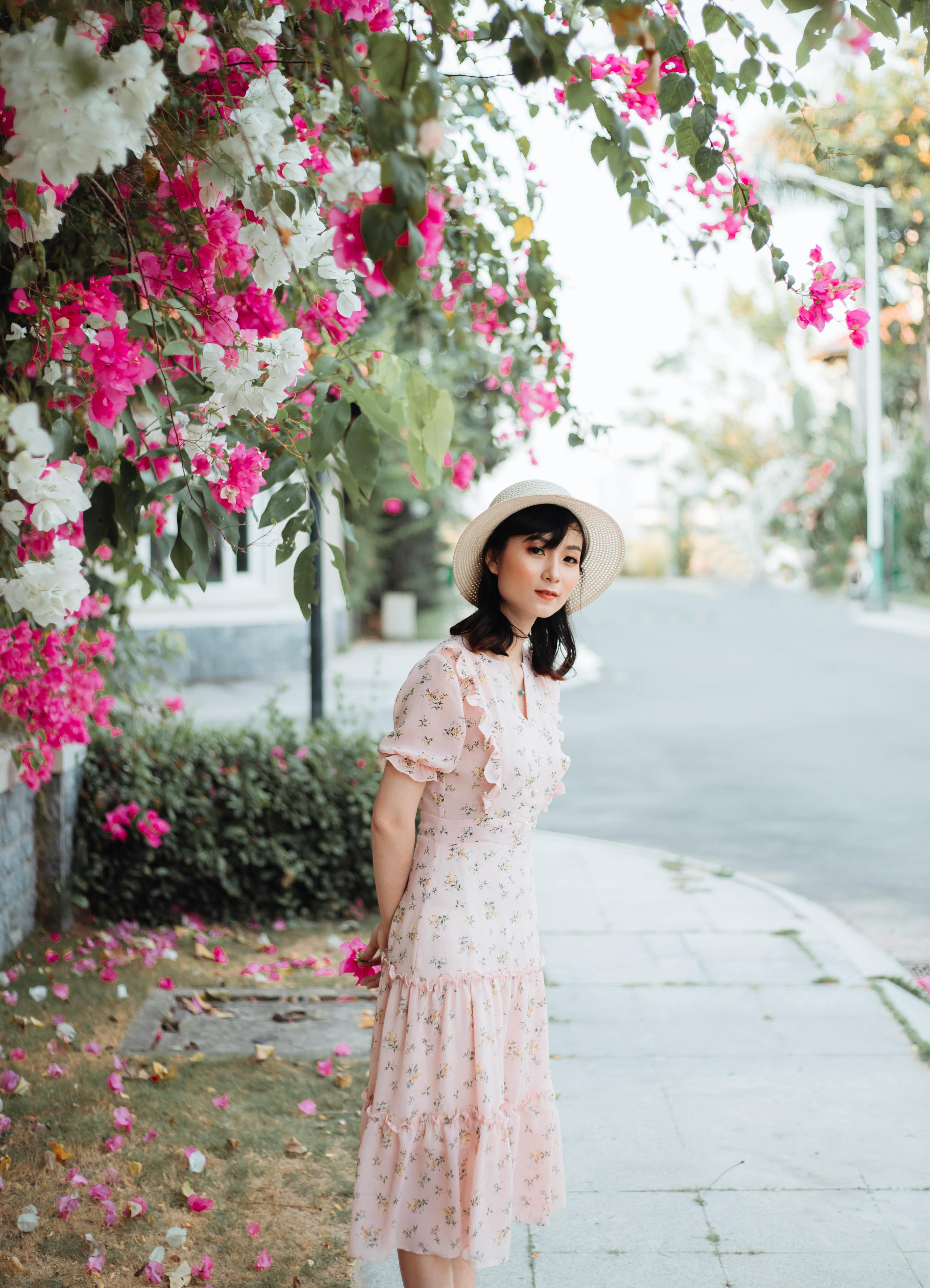 在一个阳光灿烂的日子，一位穿着粉色花衣服、戴着太阳帽的妇女站在五颜六色的花丛中