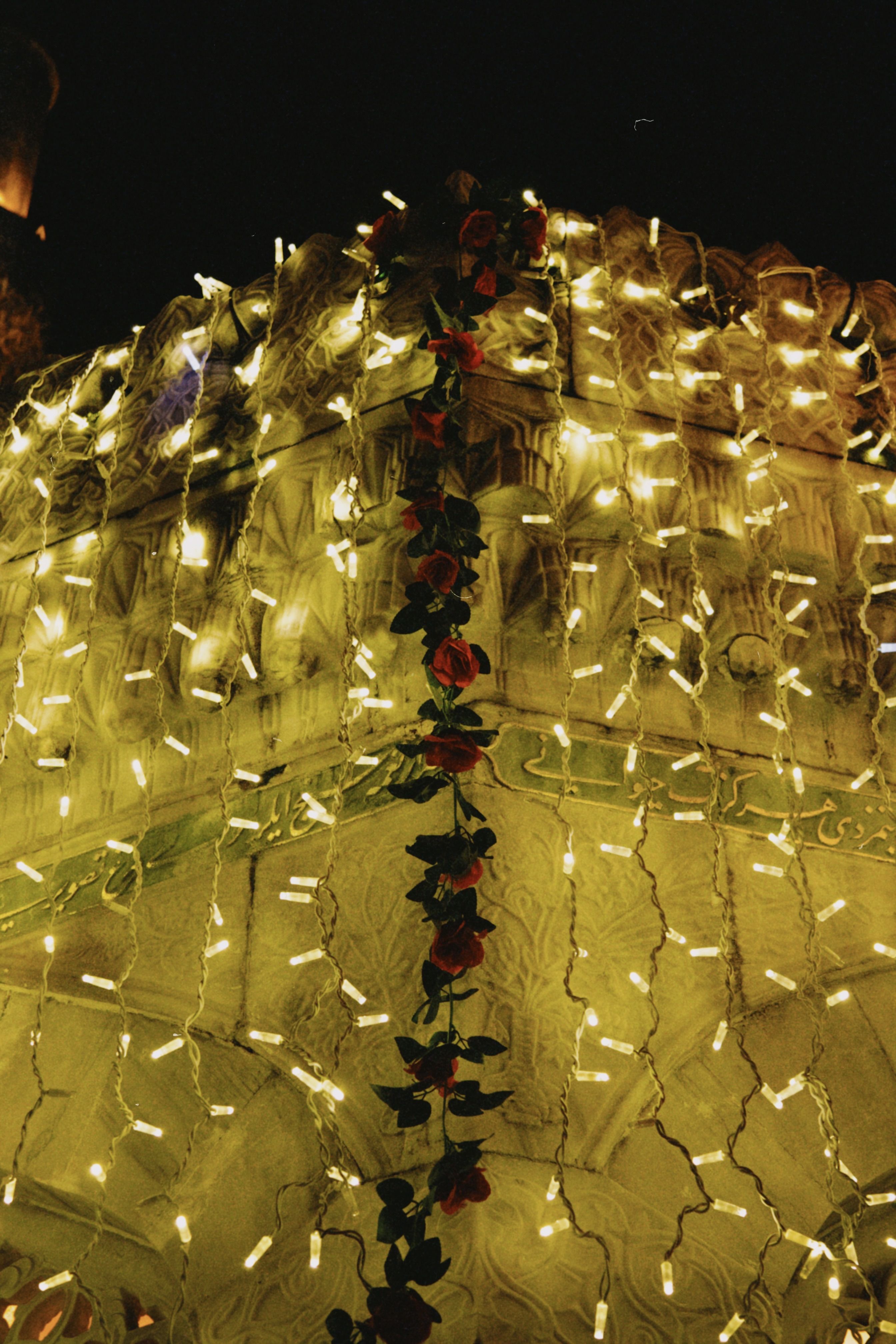 Stone facade adorned with string lights and red floral garland, glowing at night.