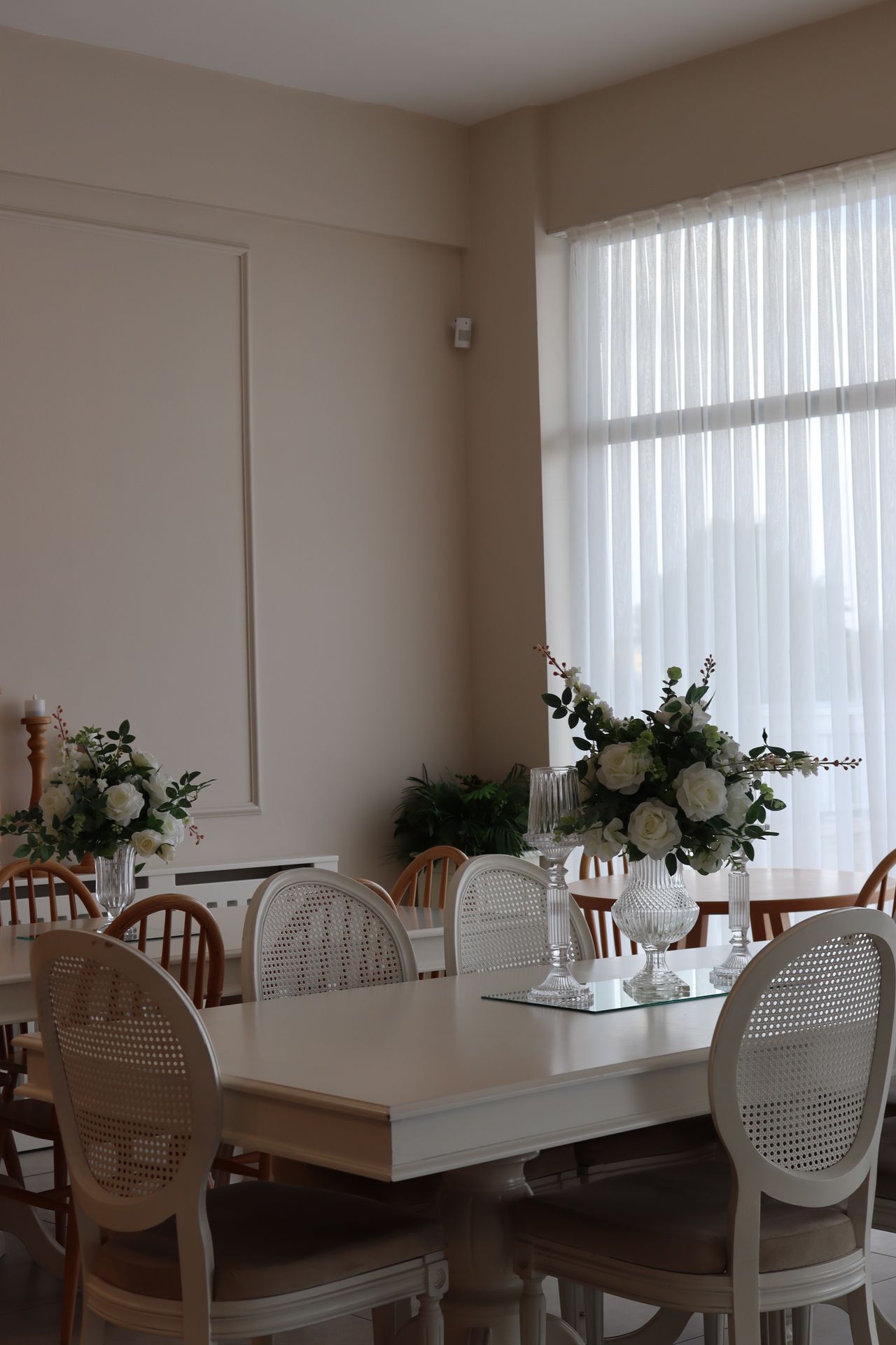 White rectangular pedestal table with cane-back chairs in a bright room