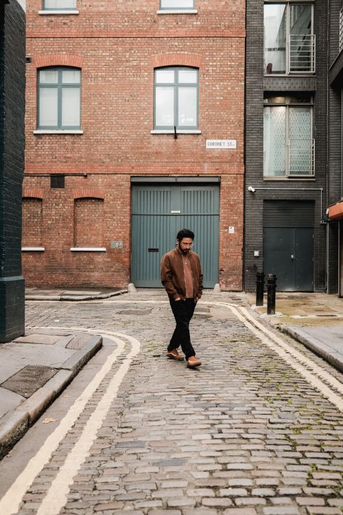 Free A man walks down a cobblestone alley in a city area, surrounded by brick buildings. Stock Photo