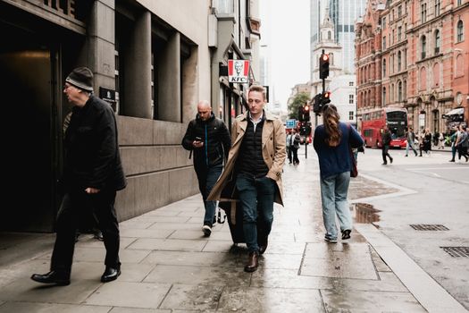 A bustling city street in London with people walking, red buses, and historic architecture.