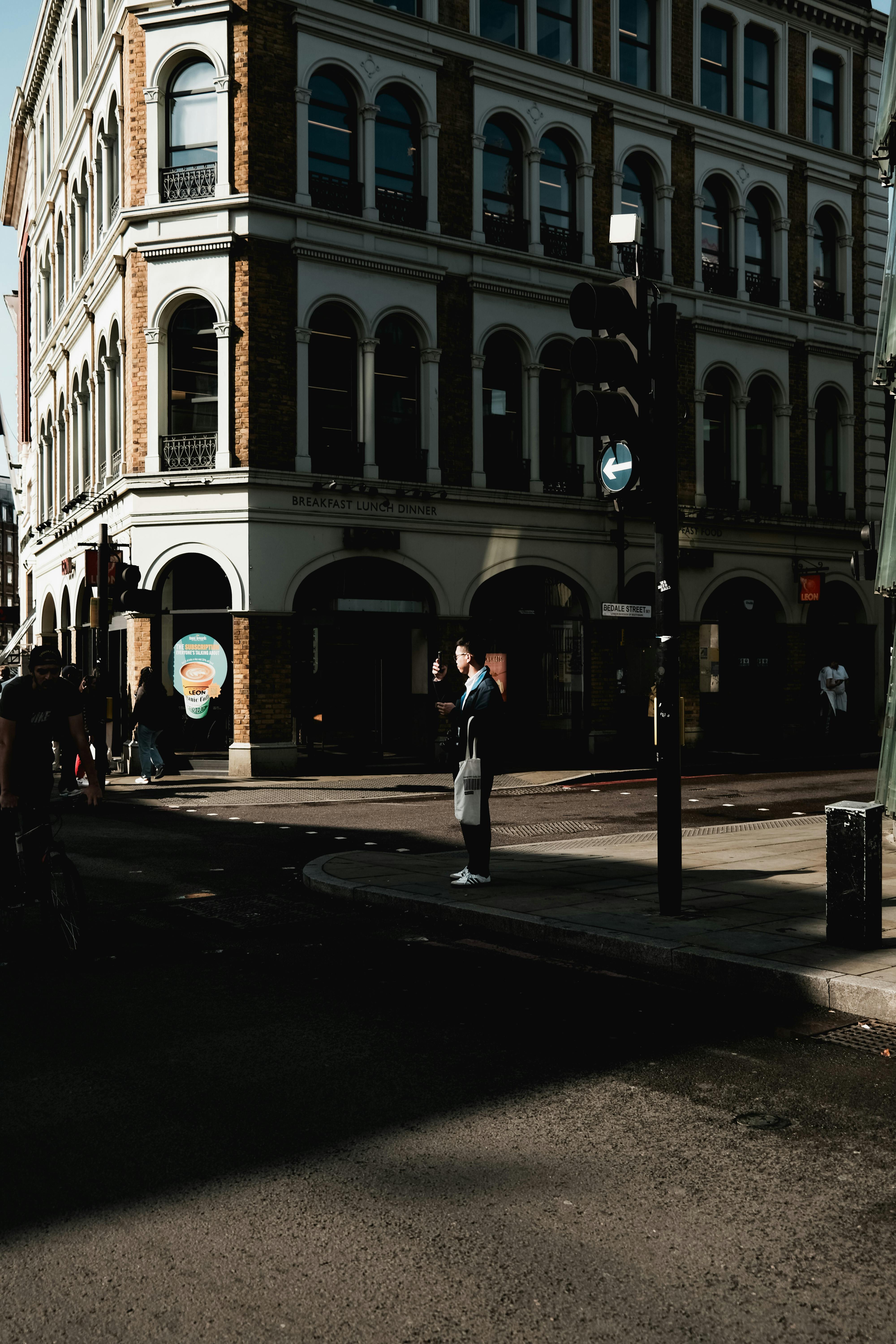 Free A person waits at a crosswalk beside a historic building in an urban setting during the day. Stock Photo