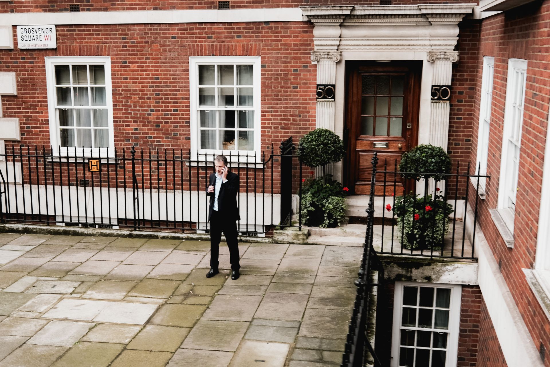 Man on phone near brick building in Grosvenor Square, London.