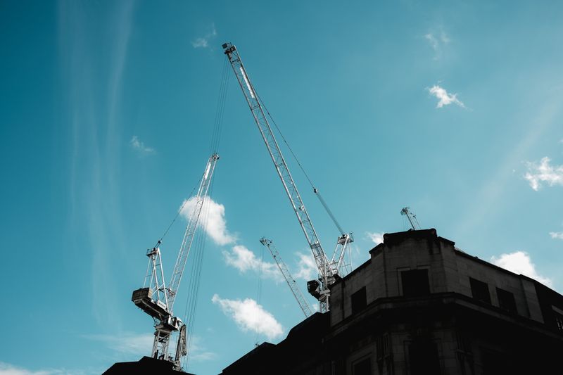 Silhouetted construction cranes extend into a clear blue sky.