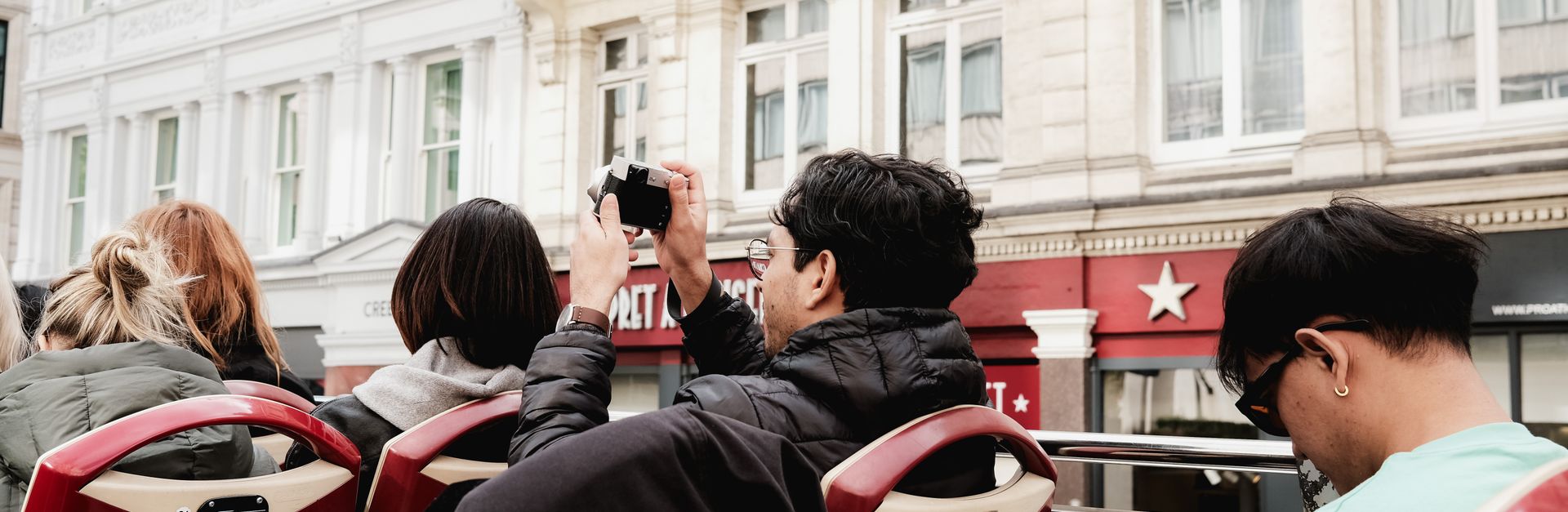 Back view of tourists on an open-top bus exploring city streets. Capturing memories.