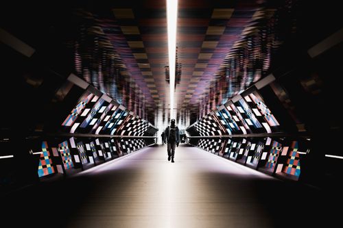 Free A person walks through a neon-lit, art-filled futuristic tunnel, creating a sense of modern mystery. Stock Photo