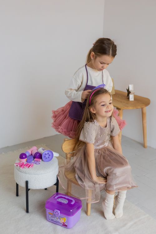 Free Two young girls play hairdresser, one styling the other's hair in a cozy indoor setting. Stock Photo
