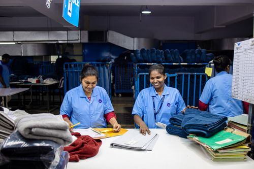 Free Two female textile workers sorting fabrics in a factory setting, wearing blue uniforms. Stock Photo
