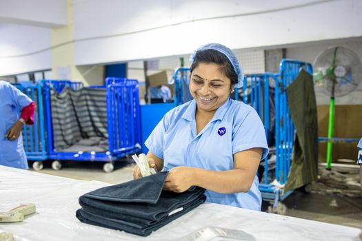A cheerful worker folding textiles in a vibrant factory environment, showcasing industrial work life.