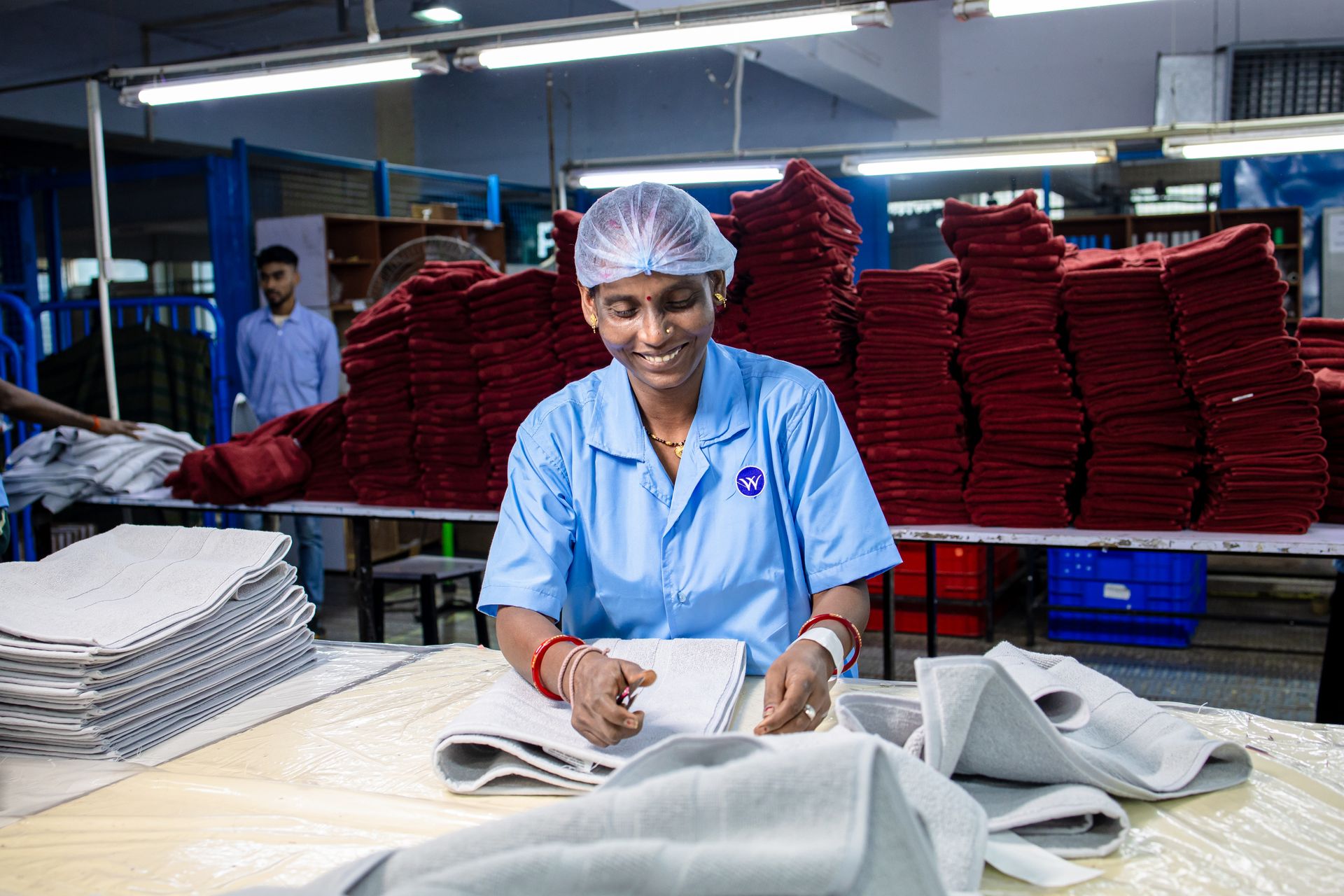 Factory worker in blue uniform smiling while sorting textiles indoors.