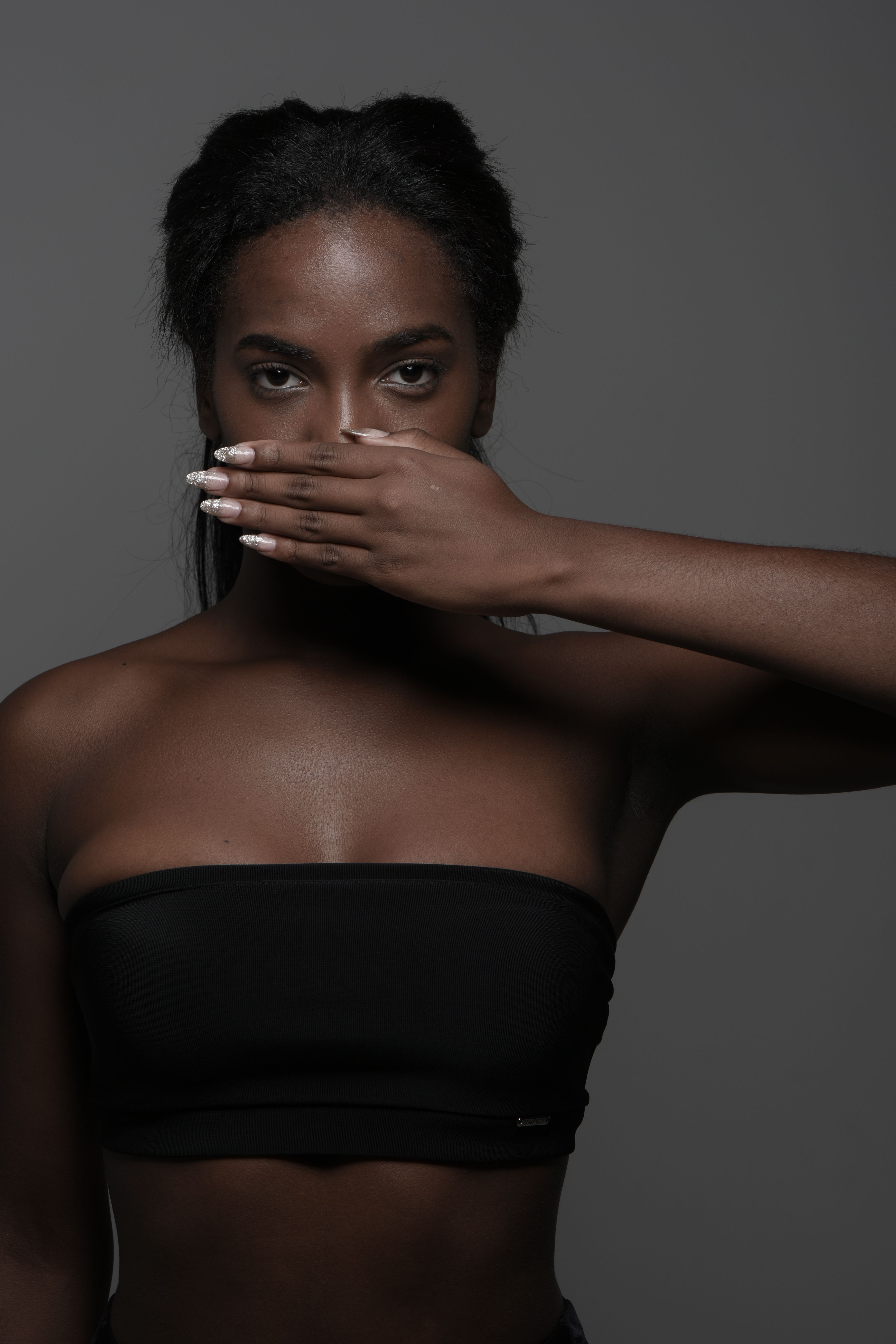Moody portrait of woman covering her mouth with hand in a dark studio.