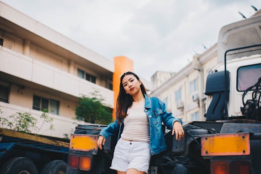 一位亚洲女性身着休闲装，在城市街道的卡车旁自信地摆着姿势，散发着现代气息