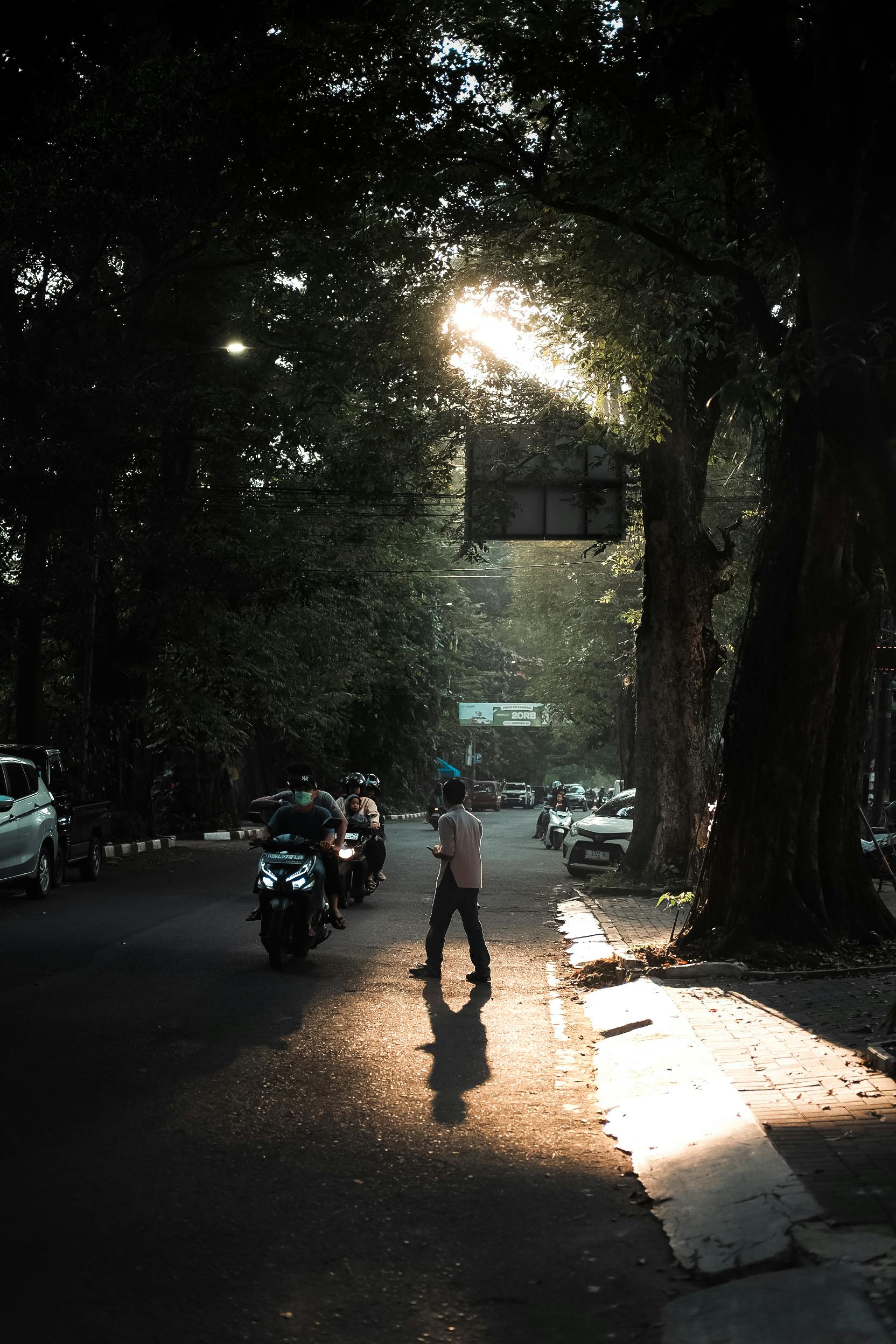 A serene street scene in Jawa Barat, Indonesia, with sunlight filtering through trees.