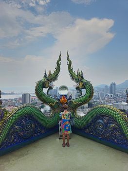 A person enjoys a panoramic view of Chonburi from a temple rooftop adorned with ornate sculptures.