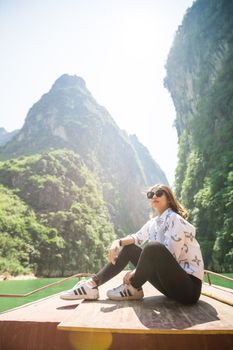 时尚的女人在风景优美的山脉间的船上享受阳光明媚的一天