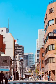 Bustling Tokyo street with people and cars under a bright blue sky.