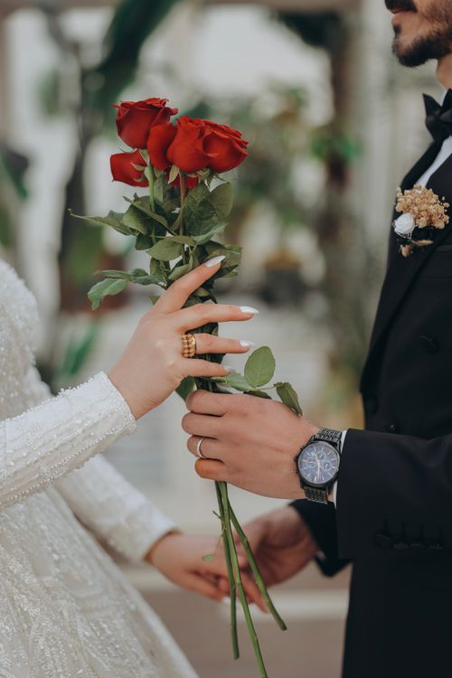 Free Elegant wedding photo capturing a bride and groom exchanging a bouquet of red roses. Stock Photo