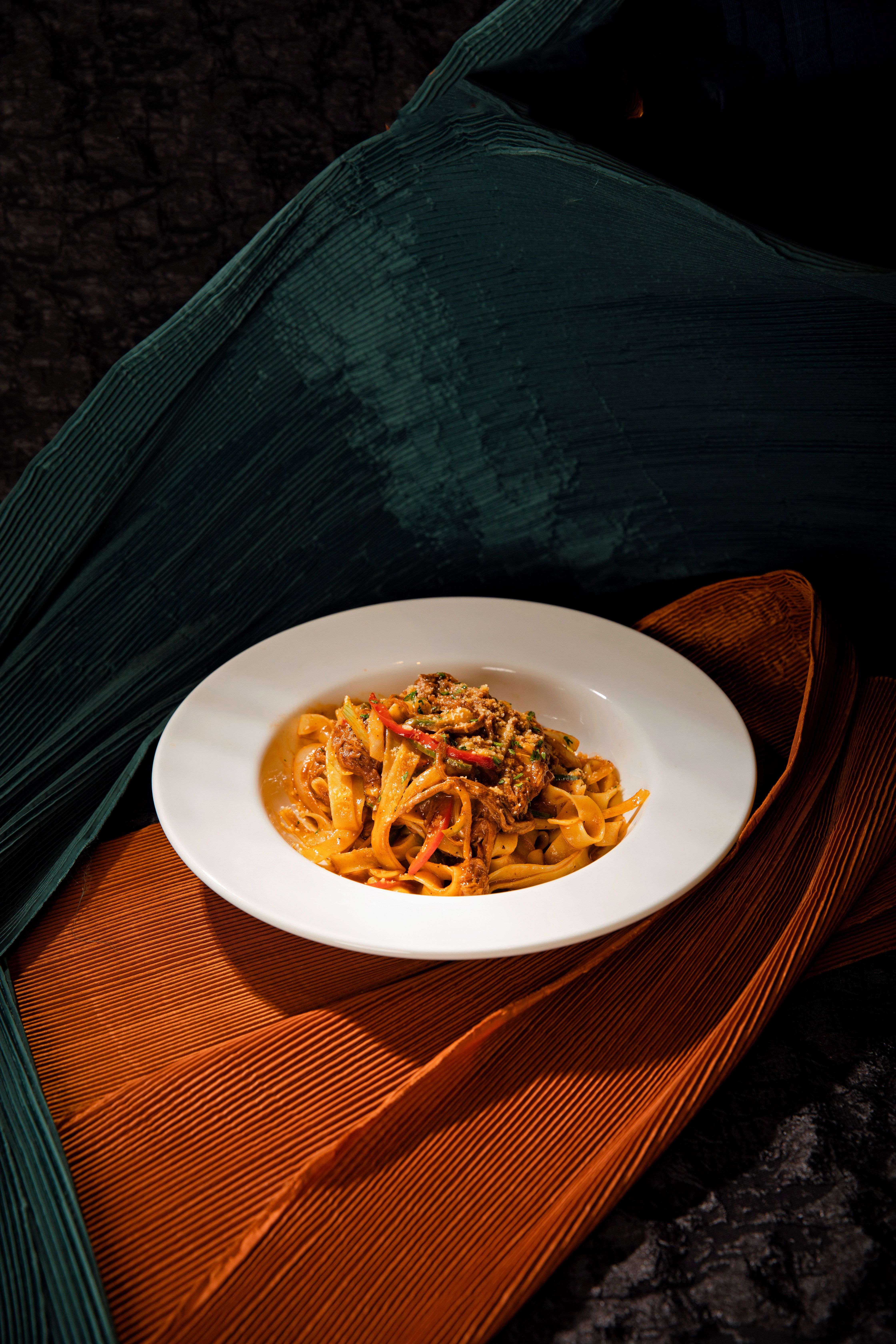 A beautifully presented spaghetti dish set against a textured green and orange fabric backdrop.