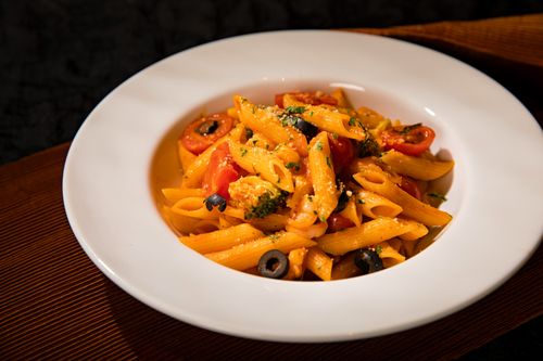Free Vibrant penne pasta with cherry tomatoes, olives, and veggies in a modern setting. Stock Photo