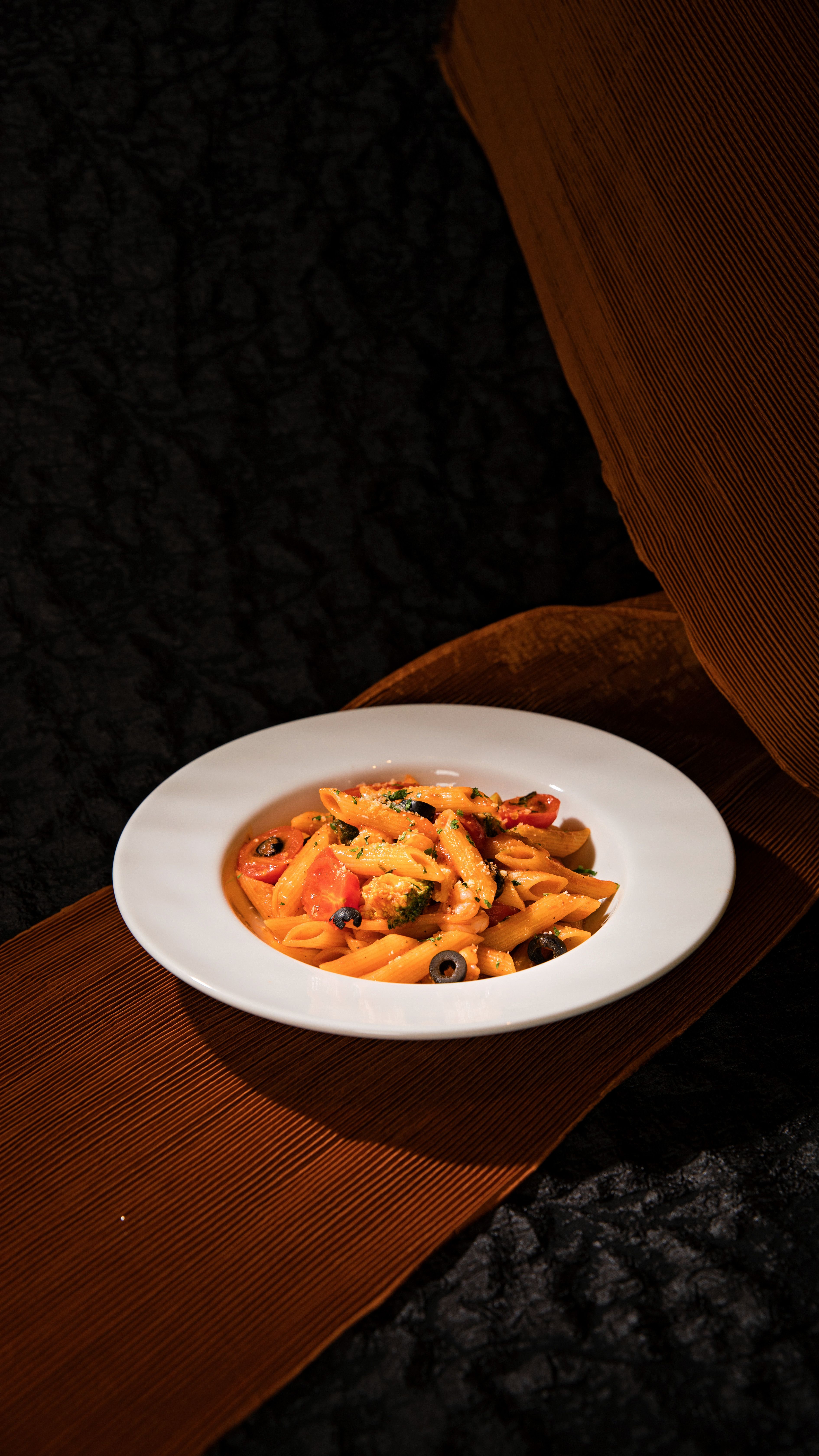 A vibrant Italian pasta dish garnished with herbs and olives presented on elegant fabric.