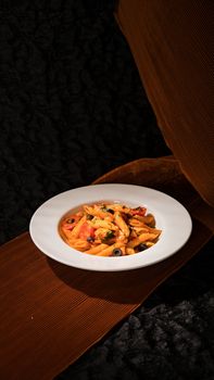 A vibrant Italian pasta dish garnished with herbs and olives presented on elegant fabric.
