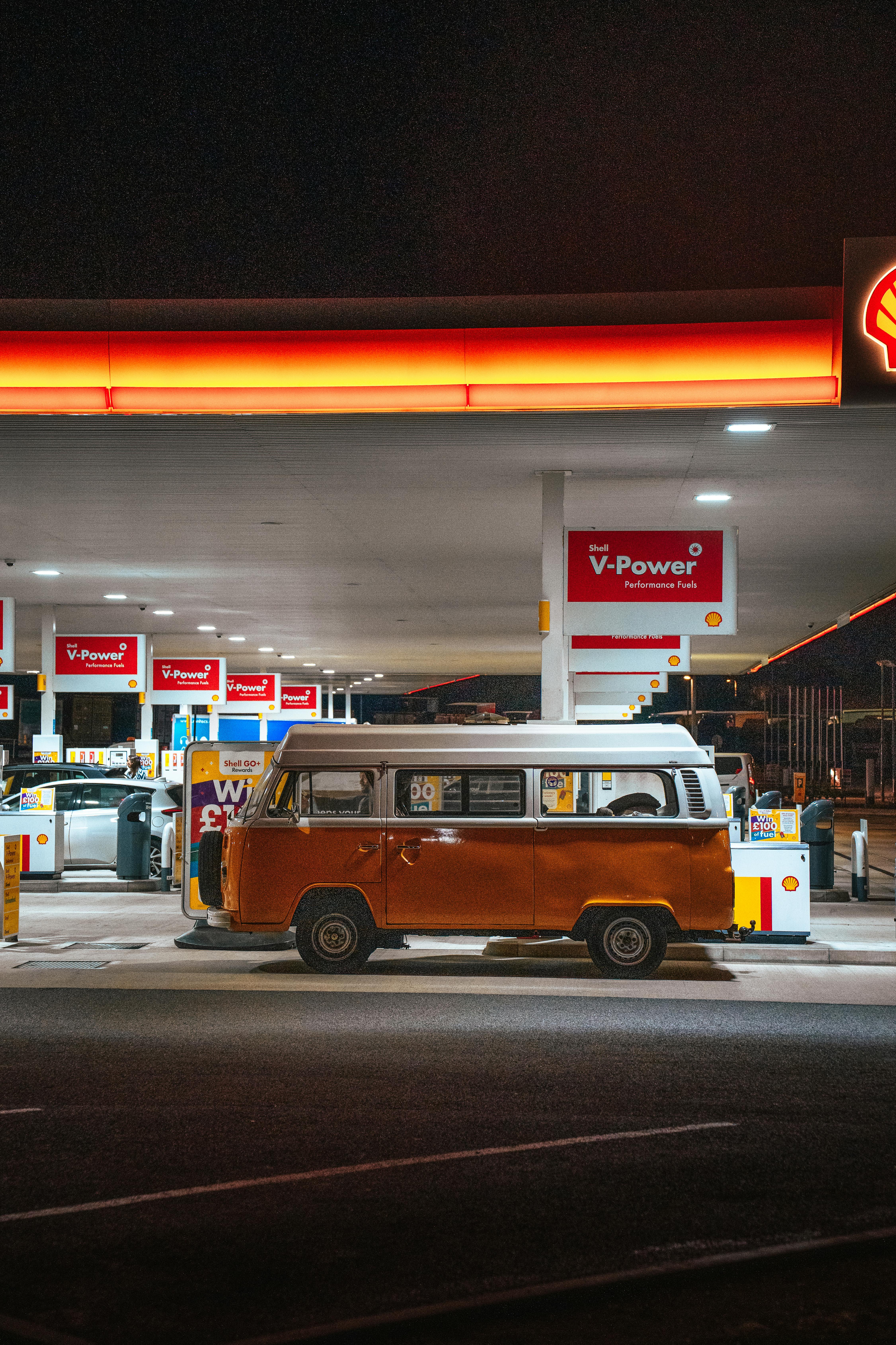 Orange vintage camper van parked at a gas station during night time.