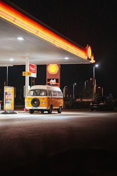 A classic orange van parked at a Shell gas station under bright lights at night.
