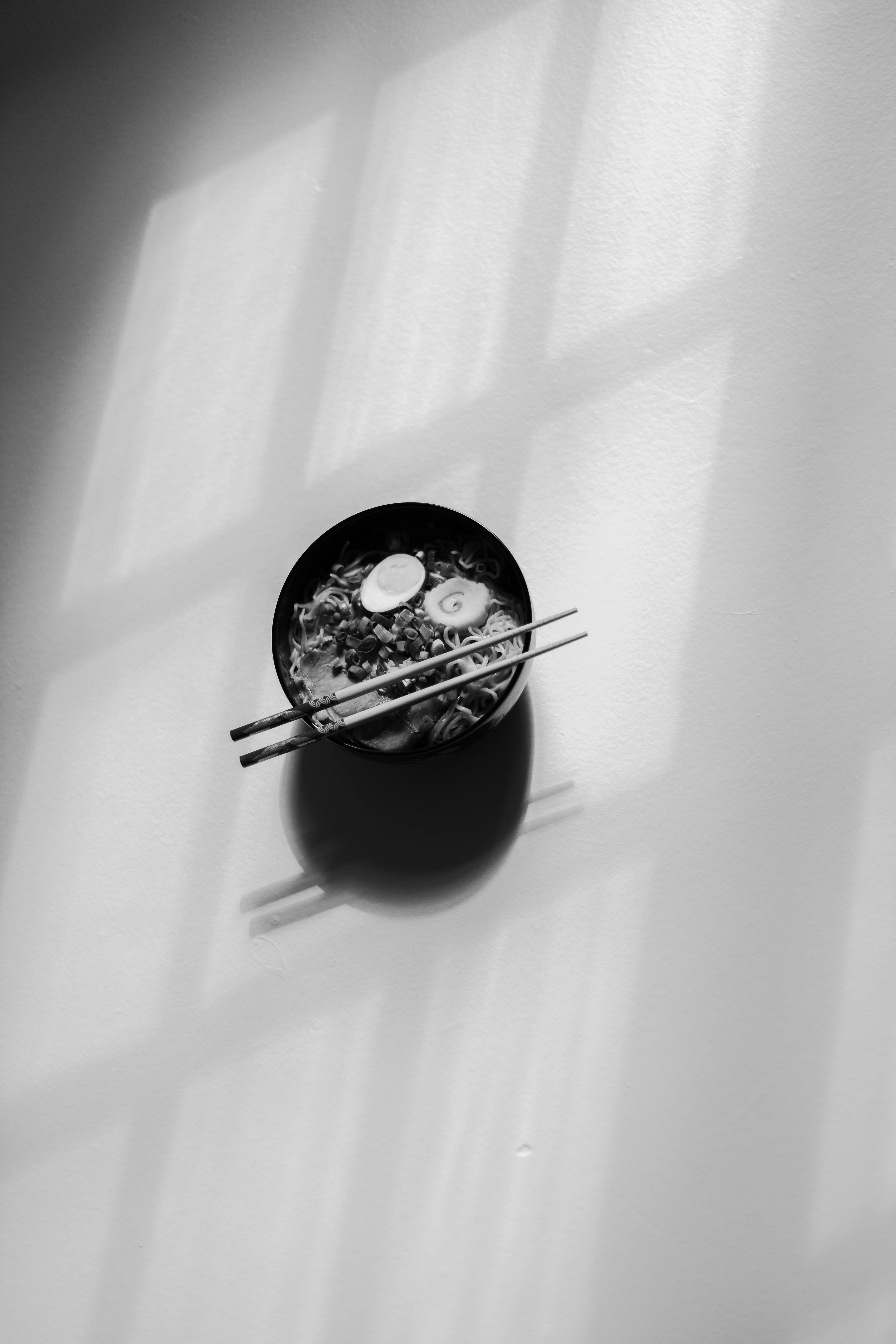 Ücretsiz Çubukların gölge oluşturduğu, minimalist bir hava yaratan ramen kasesinin siyah beyaz fotoğrafı. Stok Fotoğraflar