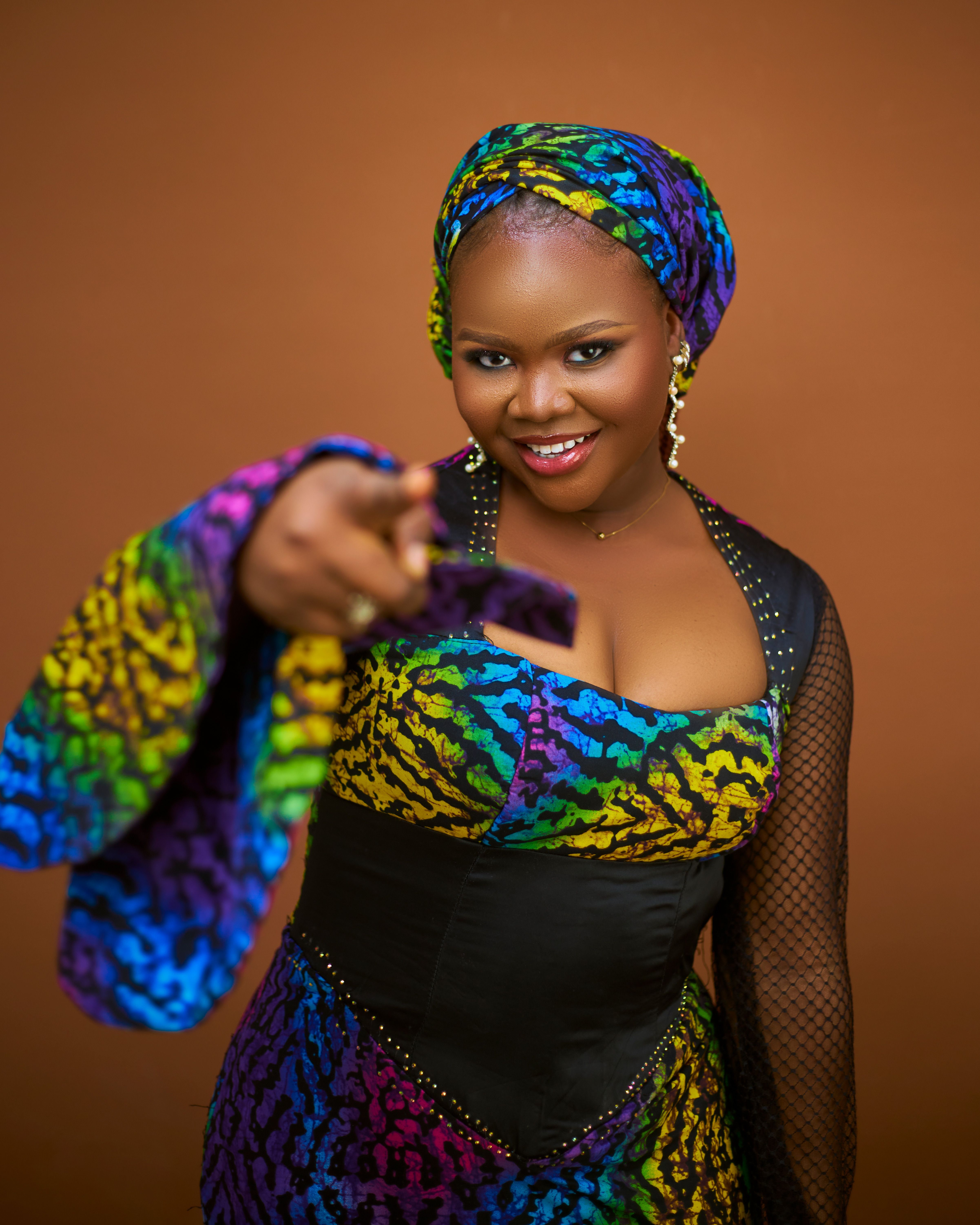 Confident woman in colorful African dress poses against a warm background.