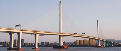 A modern cable-stayed bridge stretches over calm water against a vibrant sunset sky.