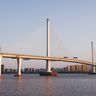 A modern cable-stayed bridge stretches over calm water against a vibrant sunset sky.