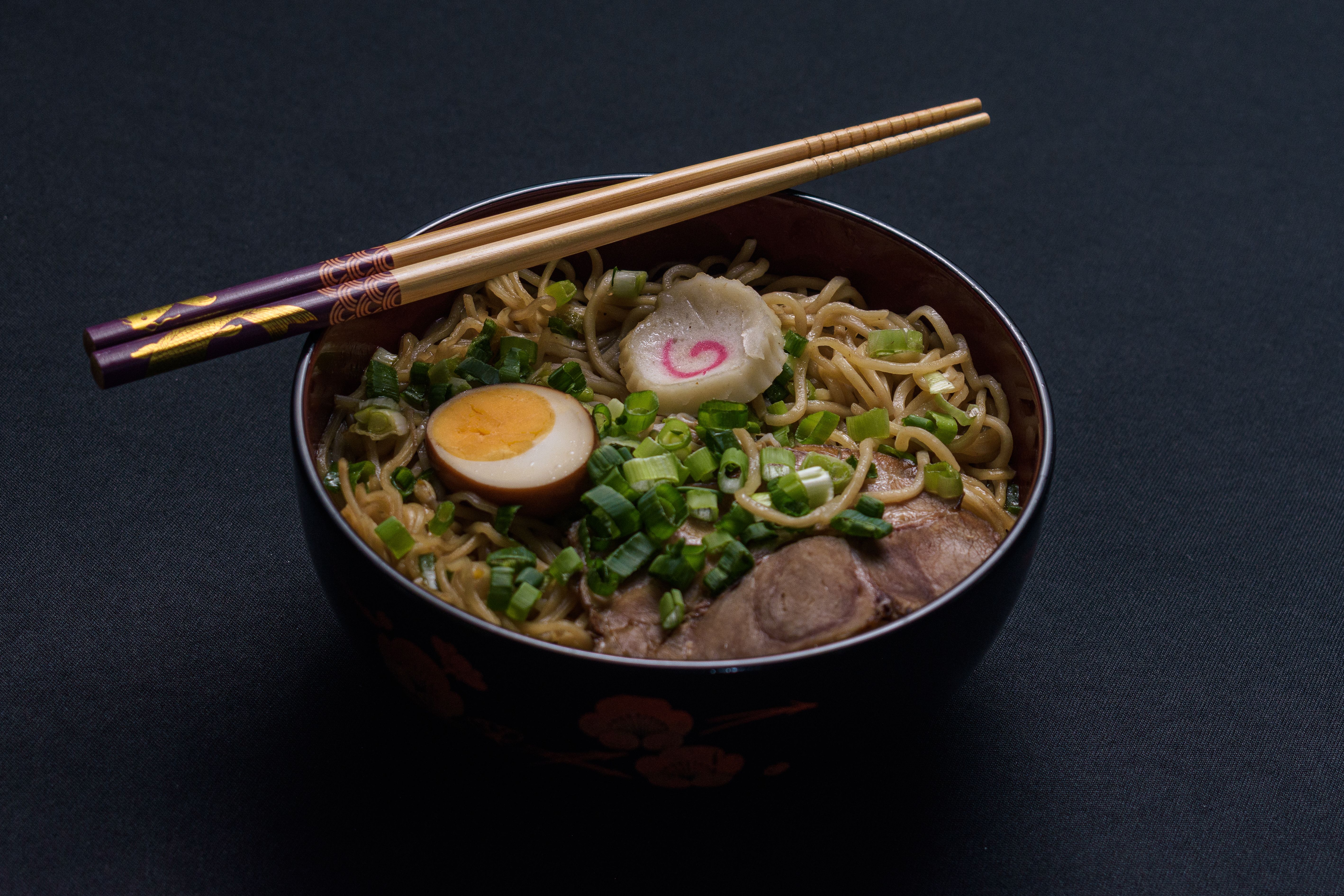 Delicious bowl of Japanese ramen with egg and scallions, topped with chopsticks.