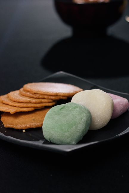 A pile of glazed brown rice crackers and pale round senbei next to a small bowl of soy sauce for dipping.