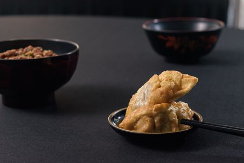 Free Appetizing fried dumplings with chopsticks served next to intricate black bowls on a black background. Stock Photo