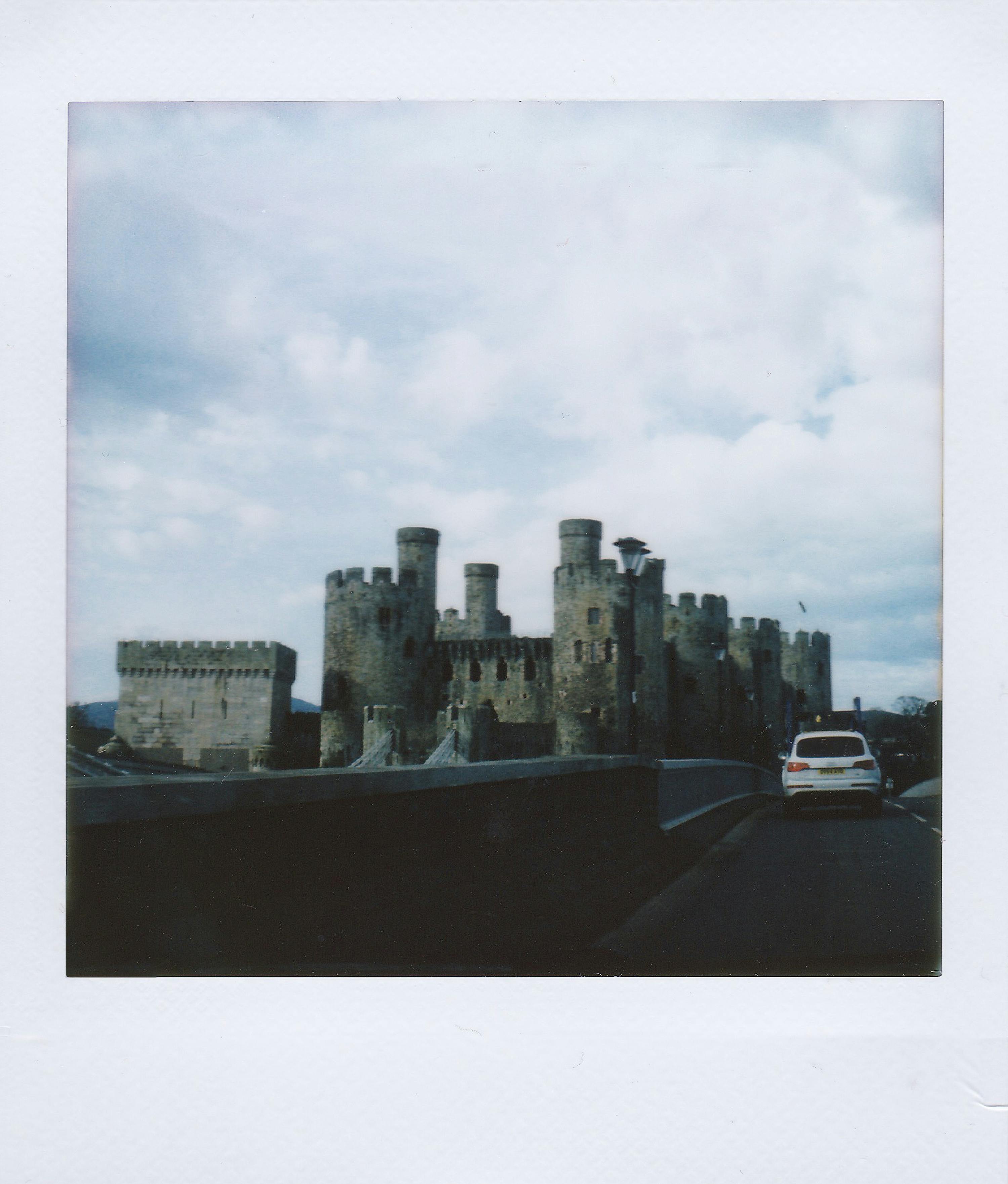 Vintage instant photo of Conwy Castle and bridge in Wales under cloudy sky.