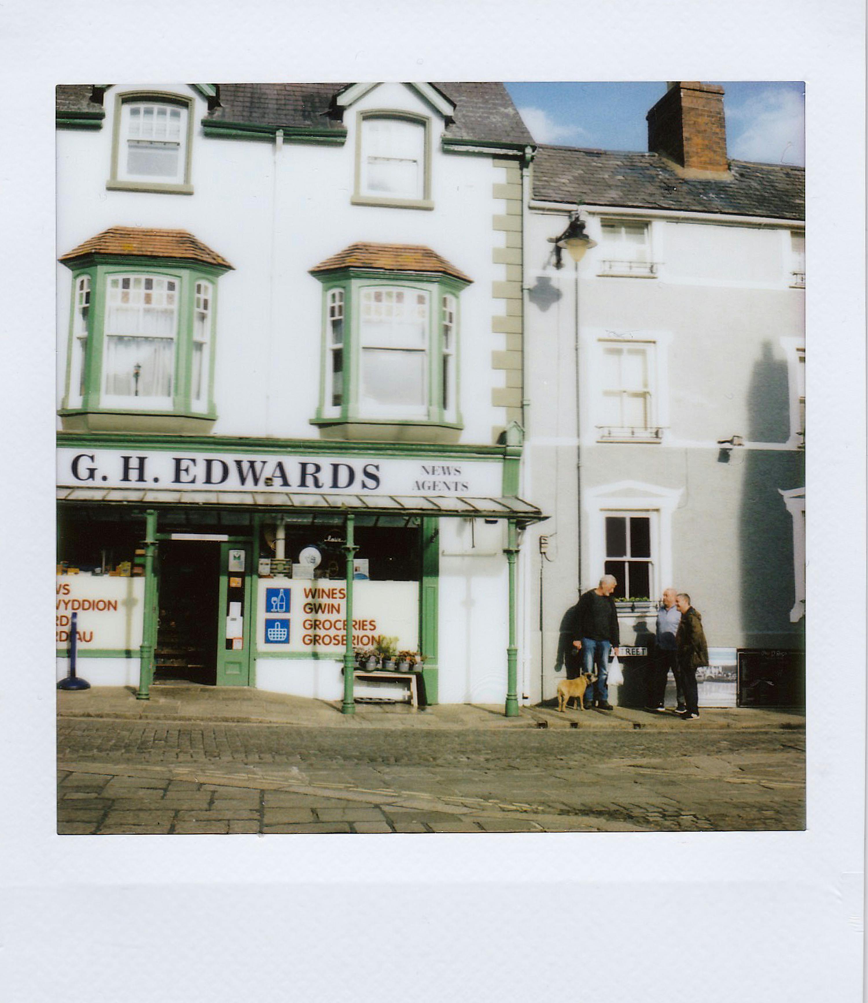 Quaint British newsagent street scene with historic architecture and passersby.