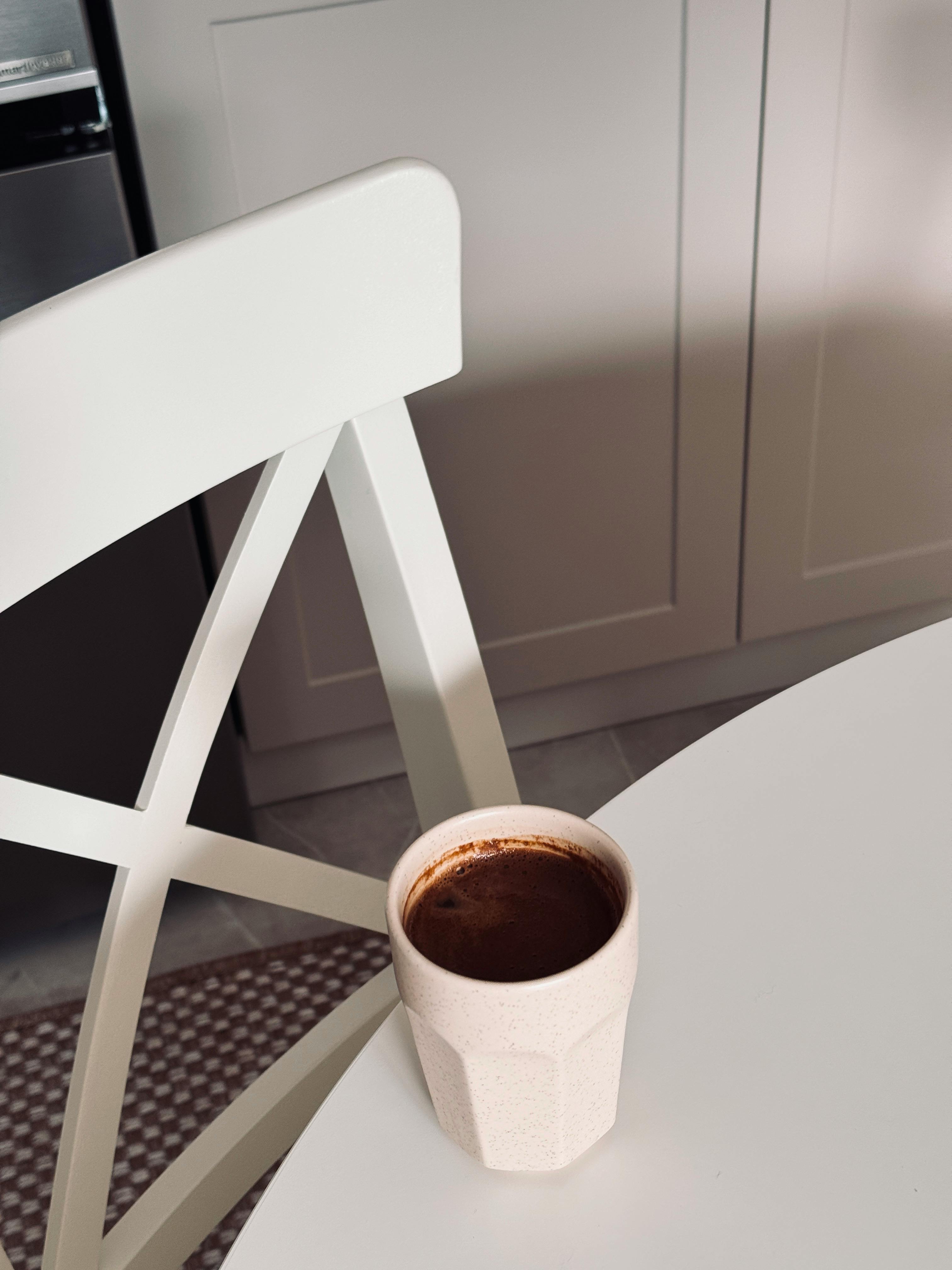 A cozy minimalist kitchen scene featuring a coffee cup on a white table, evoking warmth and relaxation.
