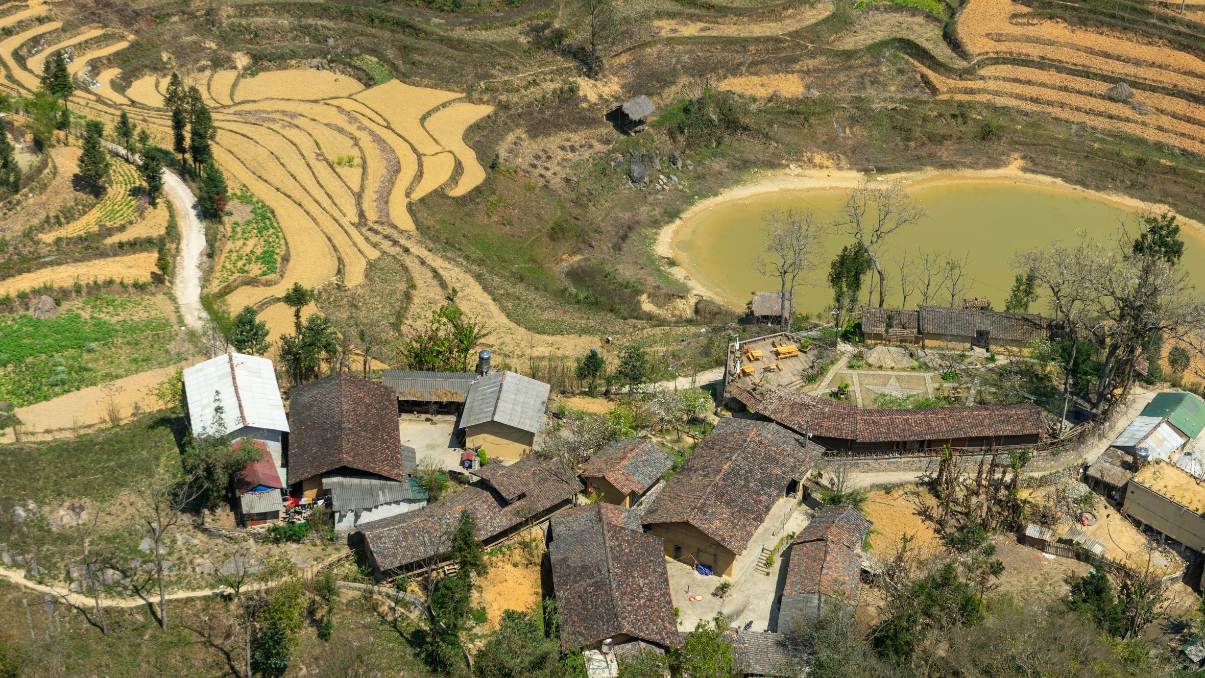 Aerial view of a village surrounded by scenic rice terraces and a small pond, capturing rural beauty.