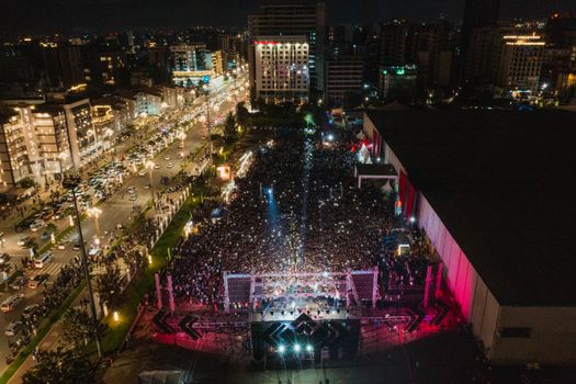 Vibrant aerial shot of a large crowd at a night city concert, illuminated by city lights.