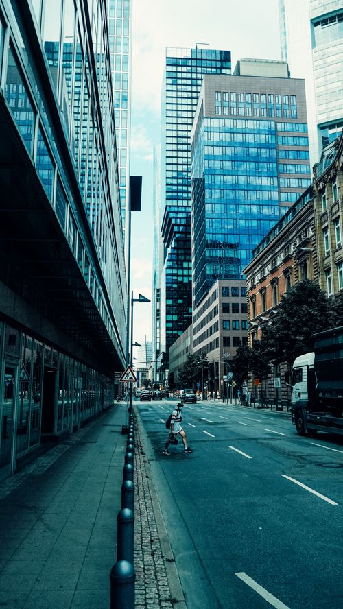Free A city street with tall glass buildings and a lone pedestrian crossing. Stock Photo