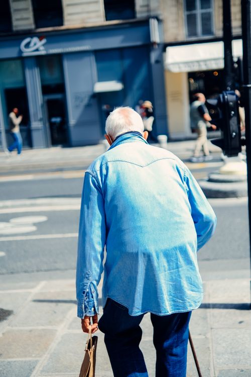 Free Senior man with a cane walks in the vibrant streets of Paris on a sunny day. Stock Photo