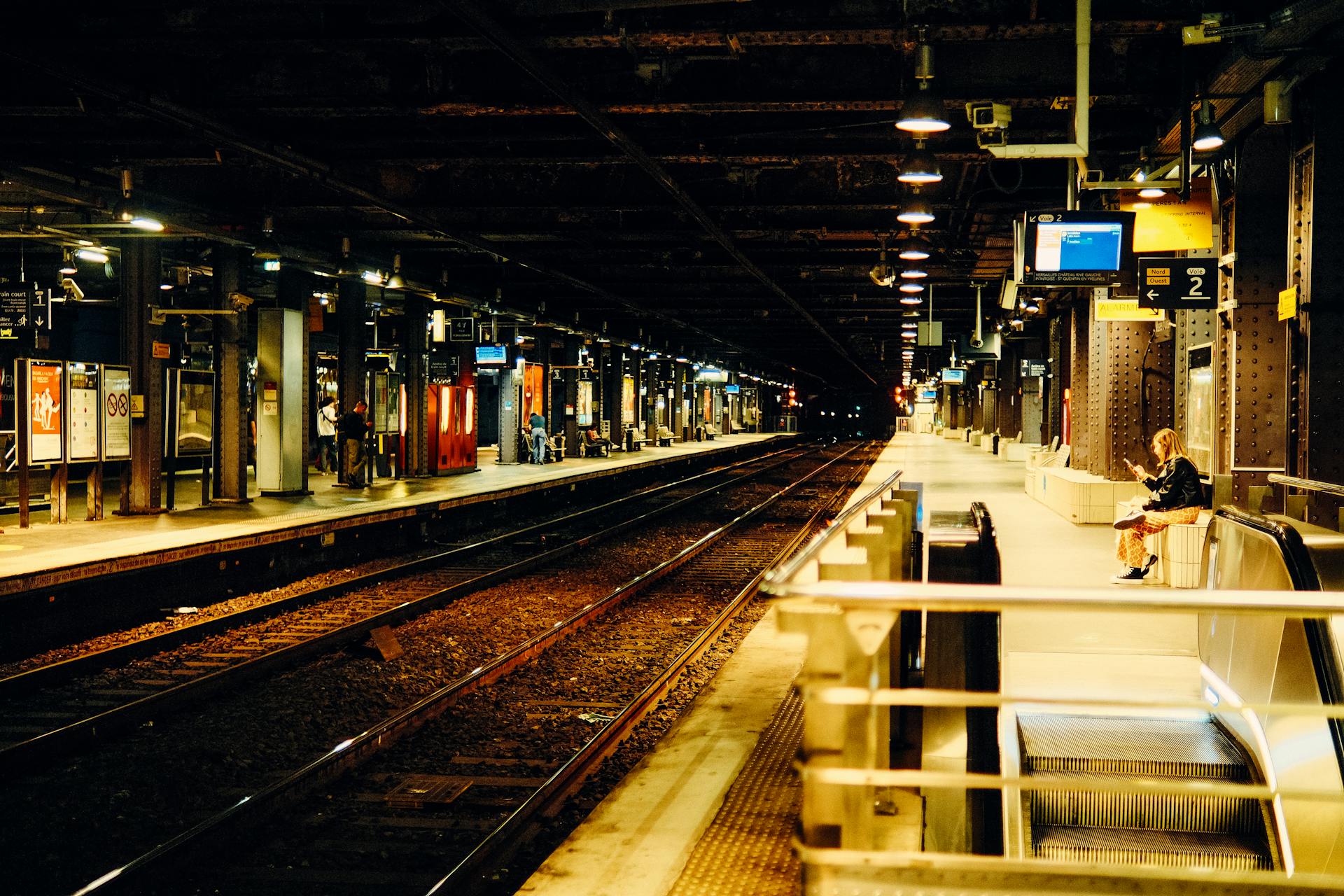 Moody ambiance in a Paris train station at night with warm lighting and a solitary person waiting.