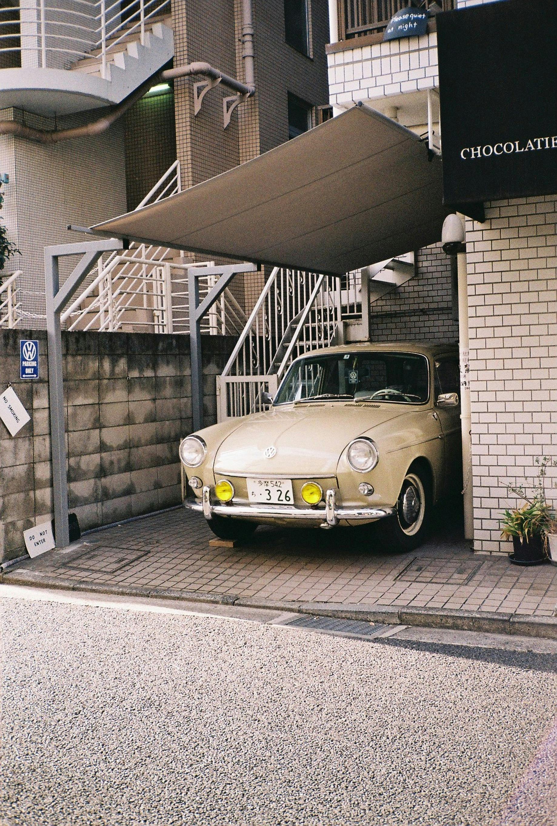Classic Volkswagen Type 3 with yellow headlights parked under a carport in urban Japan