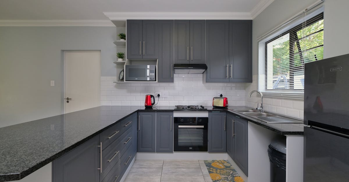 Modern kitchen featuring gray cabinetry, stainless steel appliances, including a microwave and a sleek oven, with red kettles and a black countertop, emphasizing smart appliance integration and contemporary design.